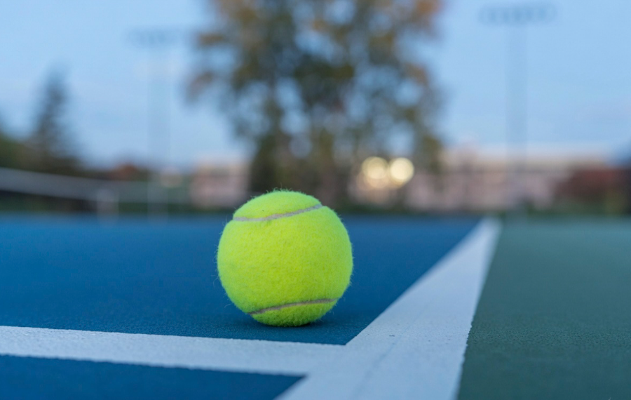 A tennis ball resting on a court baseline at dusk